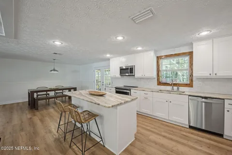 a kitchen with stainless steel appliances granite countertop a stove a sink dishwasher a microwave oven and a dining table with wooden floor