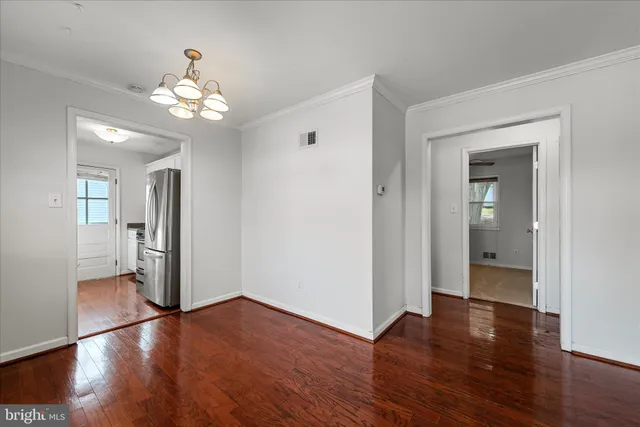 a view of an empty room with wooden floor and a kitchen