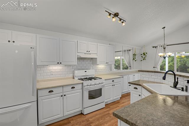 7820 Midnight Road Peyton, CO 80831 - Photo 8 of 10 Kitchen with hanging light fixtures, white cabinets, white appliances, sink, and lofted ceiling