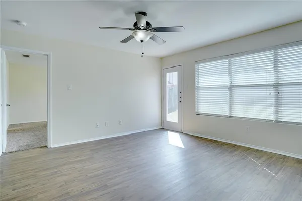 an empty room with wooden floor chandelier fan and windows