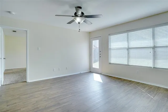 an empty room with wooden floor chandelier fan and windows