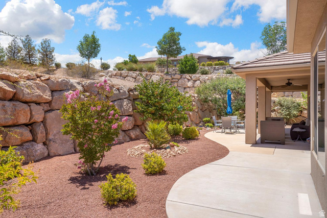 1587 Whitestone Drive St. George, UT 84790 - Photo 20 of 36 Expansive outdoor living area featuring a covered patio with ceiling fan, curved concrete pathways, and xeriscaping with mature plantings