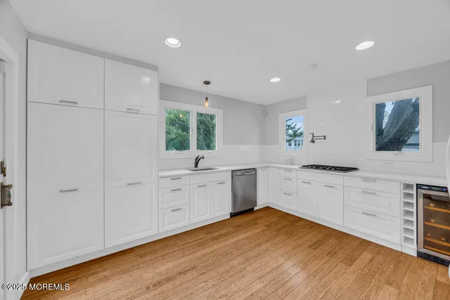 a large white kitchen with granite countertop a stove a sink and white cabinets with wooden floor