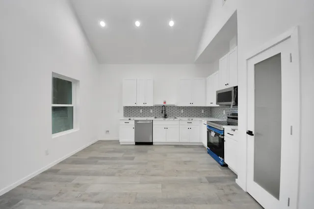 a large white kitchen with granite countertop a stove top oven a sink dishwasher and a refrigerator with wooden floor