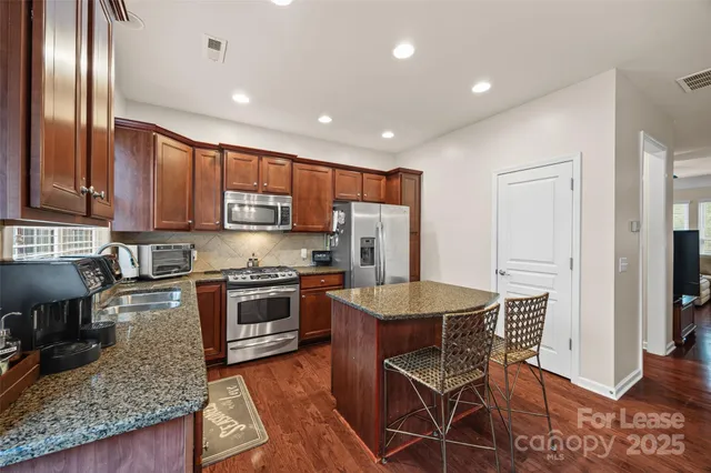 a kitchen with stainless steel appliances granite countertop a refrigerator a stove top oven and a sink with wooden floor