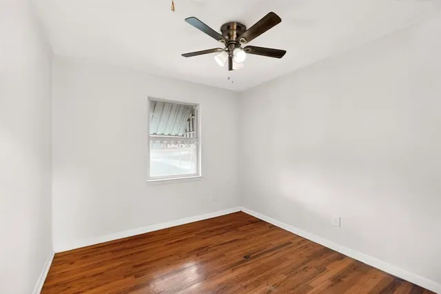 an empty room with wooden floor and a ceiling fan