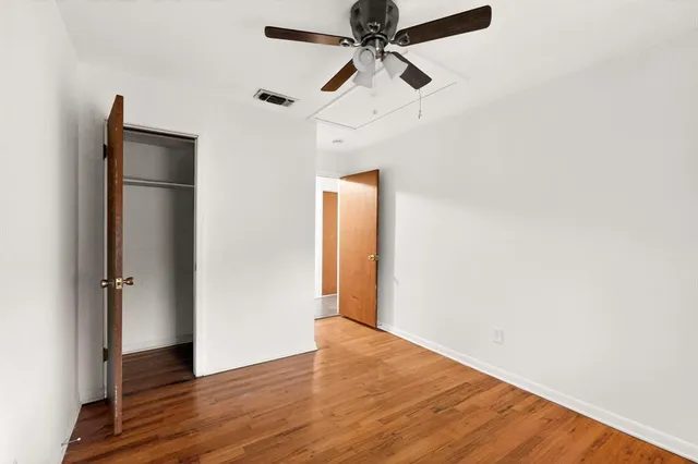 an empty room with wooden floor closet and fan