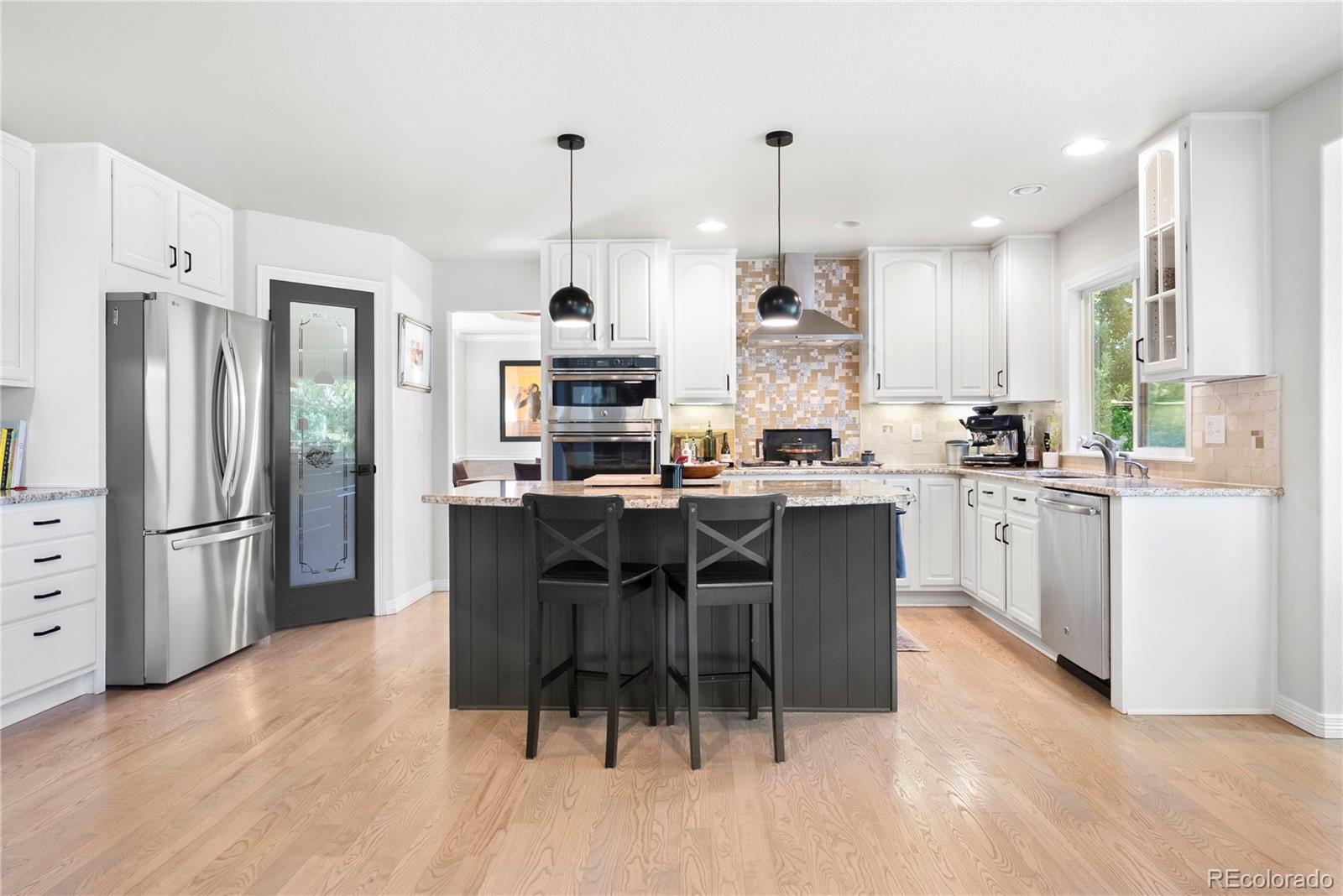 3822 Broadmoor Loop Broomfield, CO 80023 - Photo 20 of 50 a kitchen with stainless steel appliances kitchen island granite countertop a refrigerator a stove a sink a dining table and chairs with wooden floor