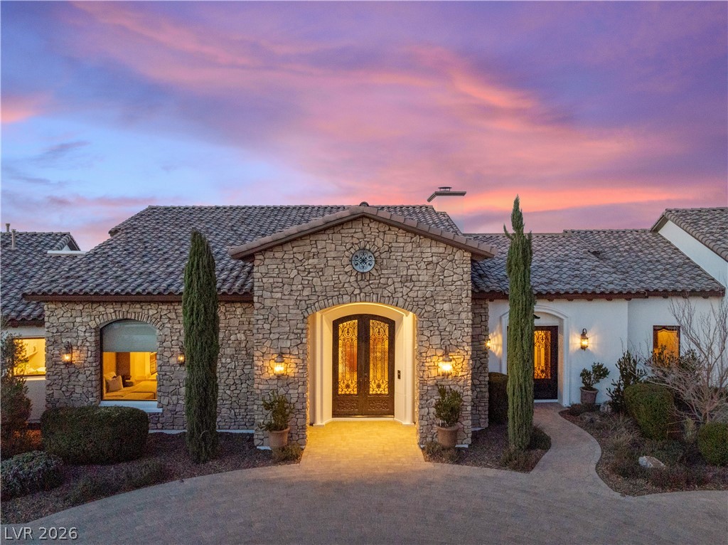 1123 Christian Road Henderson, NV 89002 - Photo 80 of 94 Grand stone and stucco facade with a tile roof, framed by mature landscaping, awaits your arrival.