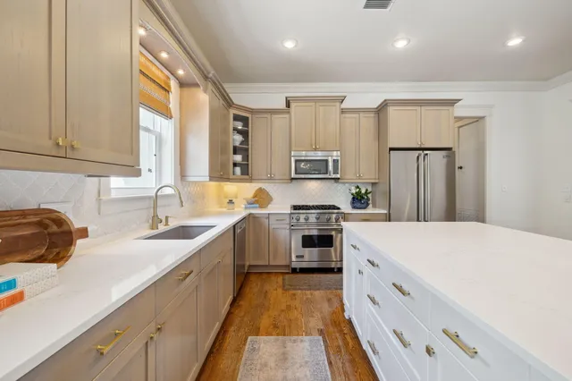 a large white kitchen with stainless steel appliances granite countertop a stove a sink a refrigerator and white cabinets with wooden floor