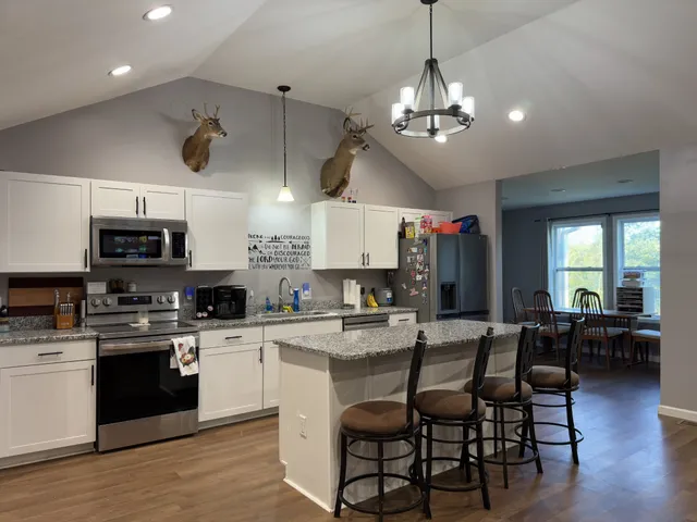 a kitchen with stainless steel appliances kitchen island granite countertop a stove top oven a sink a dining table and chairs with wooden floor