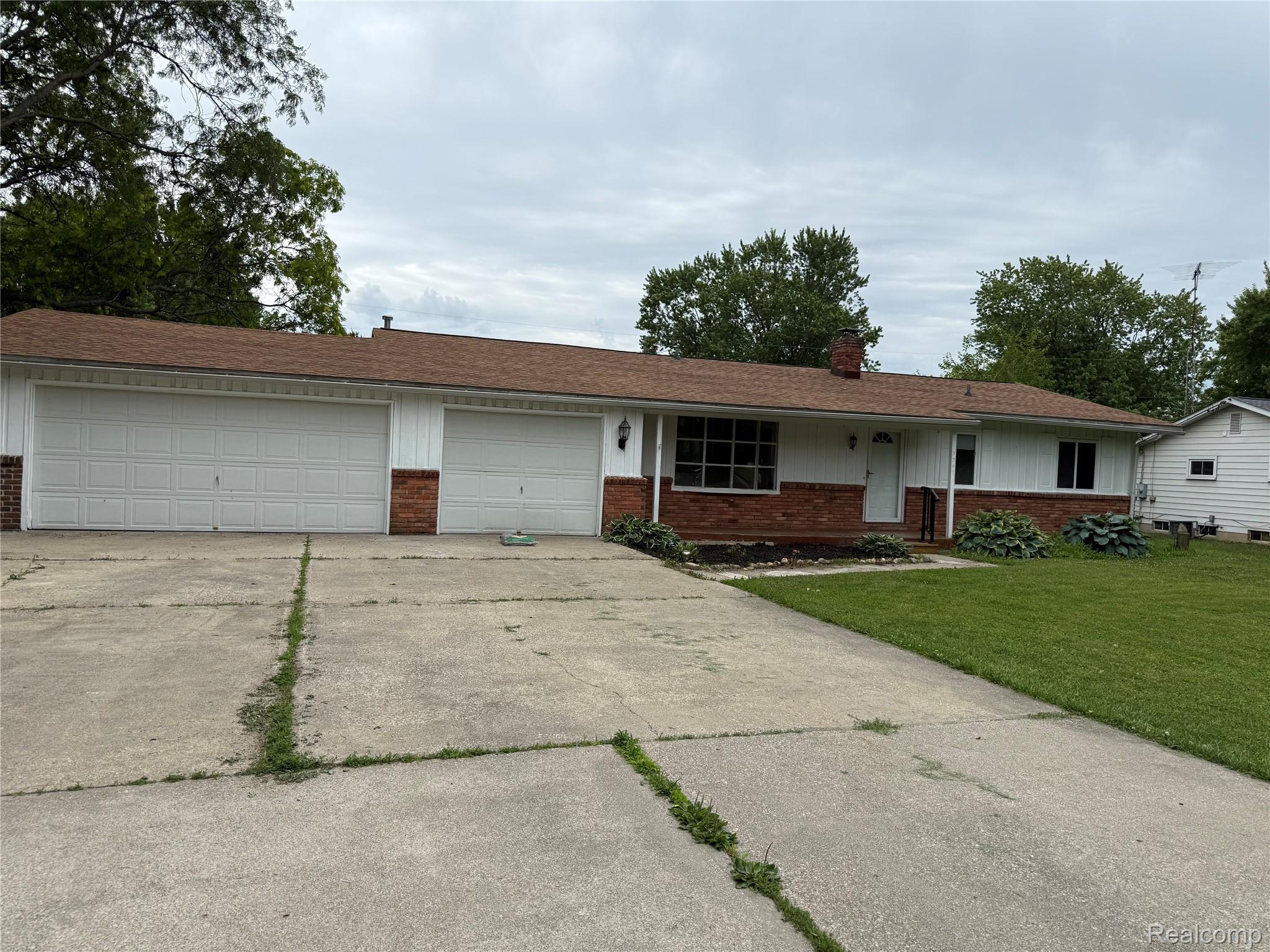 Ranch-style exterior featuring a red brick facade with white siding and a brown shingle roof