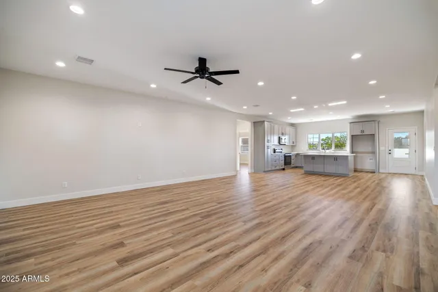 a view of an empty room with wooden floor and a ceiling fan