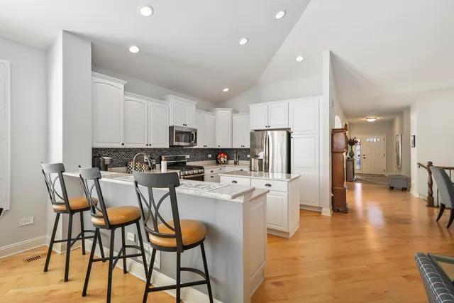 a kitchen with stainless steel appliances kitchen island granite countertop a dining table chairs refrigerator and sink