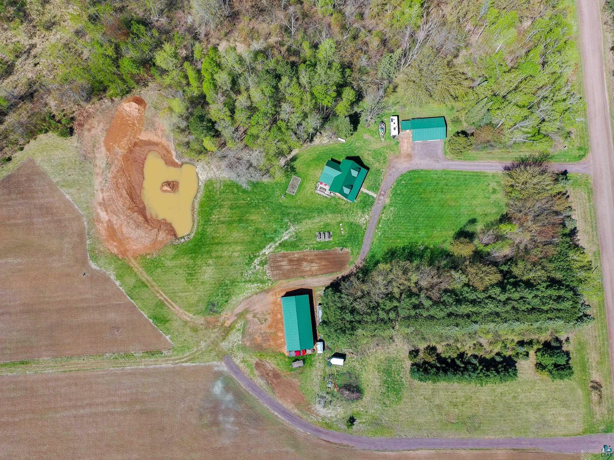 37590 Degerstrom Road Askov, MN 55704 - Photo 4 of 53 Expansive property featuring a central residence with a green metal roof, a secondary detached building, a pond with an island, and surrounding wooded areas
