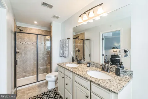 a bathroom with a granite countertop sink a toilet a mirror and shower