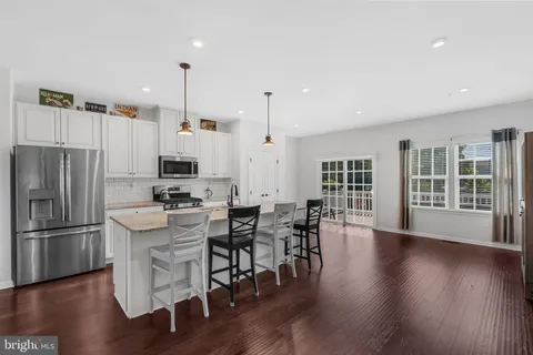 a kitchen with stainless steel appliances granite countertop a refrigerator a stove a dining table and chairs with wooden floor