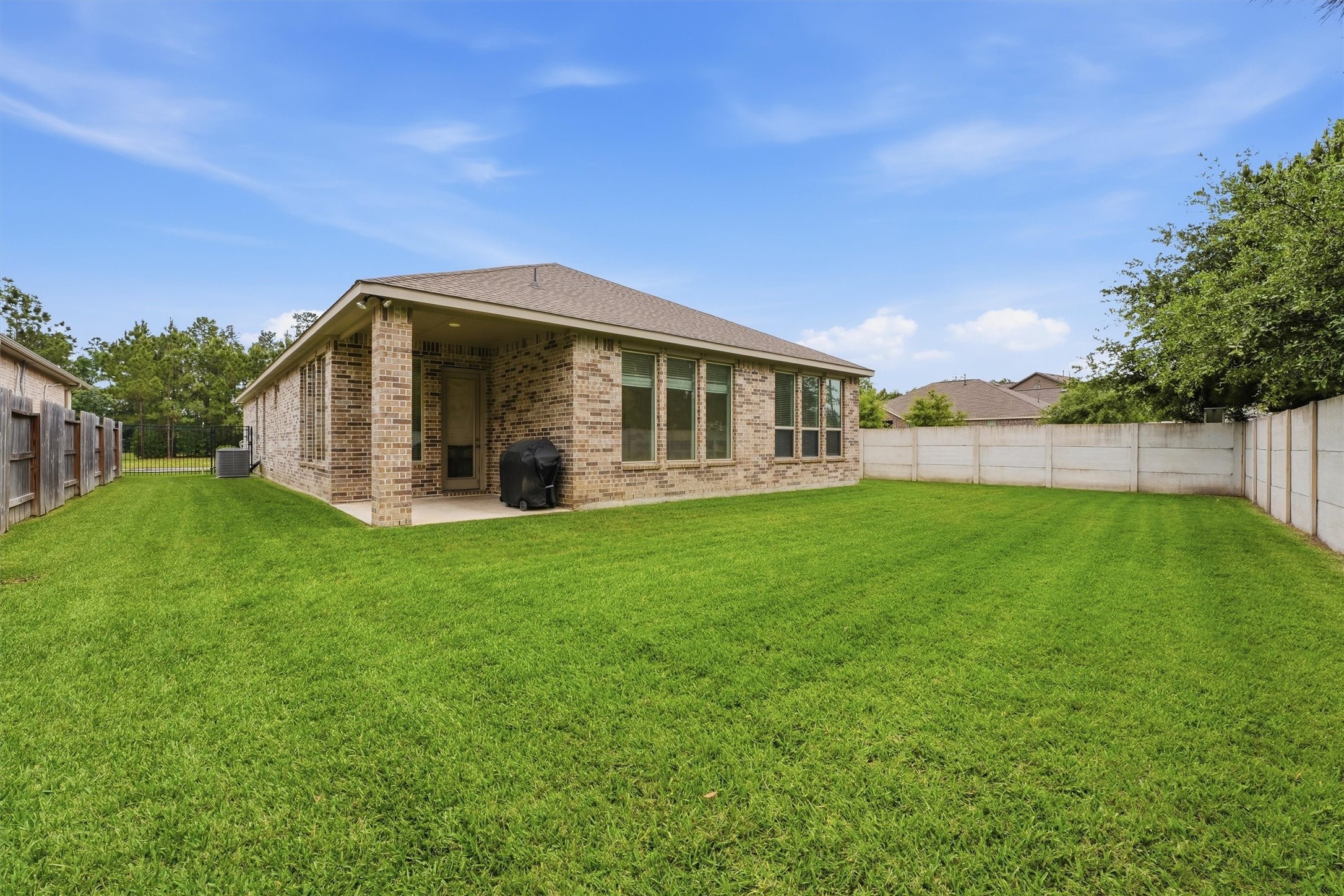 6071 Windward Falls Way Porter, TX 77365 - Photo 26 of 33 This is a spacious backyard featuring a well-maintained lawn and a brick house with large windows and a covered patio. Ideal for outdoor activities and relaxation, with privacy fencing on both sides.