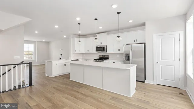 a large kitchen with stainless steel appliances kitchen island a refrigerator a sink dishwasher a stove and white cabinets with wooden floor