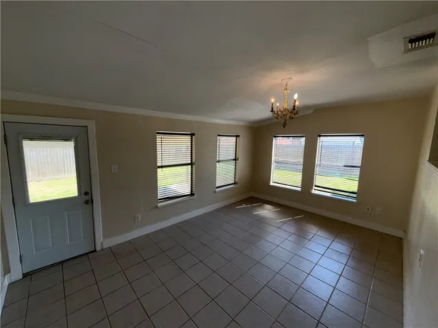 an empty room with kitchen view and a chandelier fan