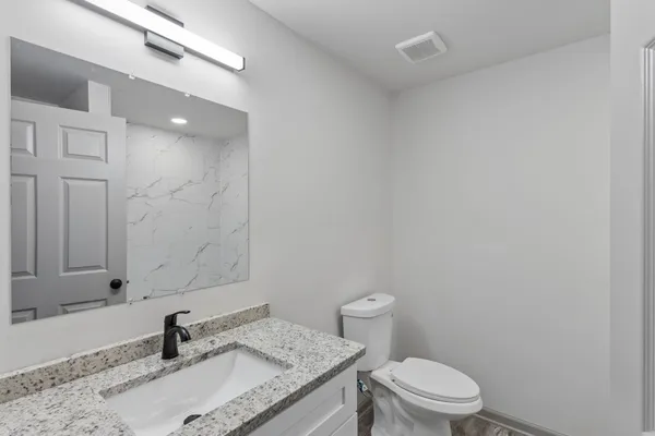 a bathroom with a granite countertop sink a toilet and a mirror