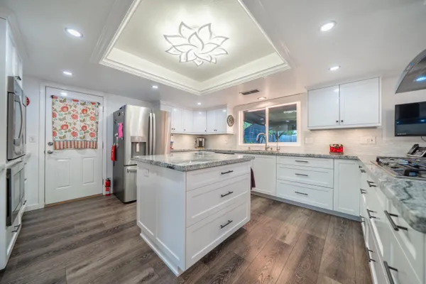 a kitchen with granite countertop a white stove top oven a chimney wooden floor and cabinets