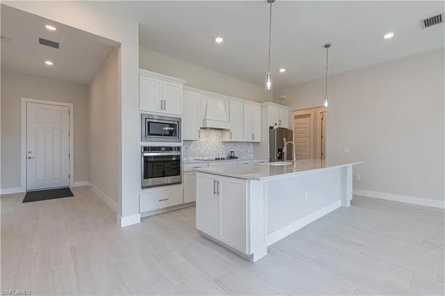 a large white kitchen with stainless steel appliances granite countertop a large counter top a sink and a stove