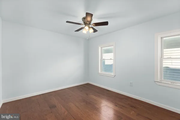 an empty room with wooden floor fan and windows