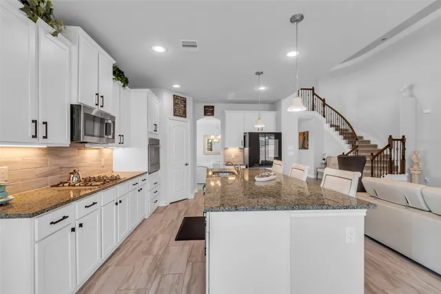 a kitchen with stainless steel appliances granite countertop a stove a refrigerator a kitchen island a sink white cabinets and chairs