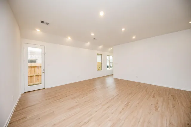 an empty room with wooden floor kitchen view and a window