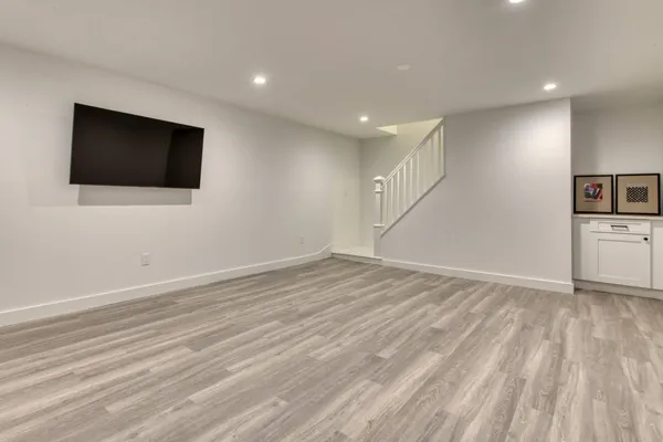 a view of an empty room with wooden floor and a kitchen