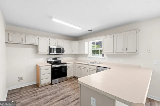 a kitchen with stainless steel appliances granite countertop a stove top oven a sink a refrigerator white cabinets and wooden floor