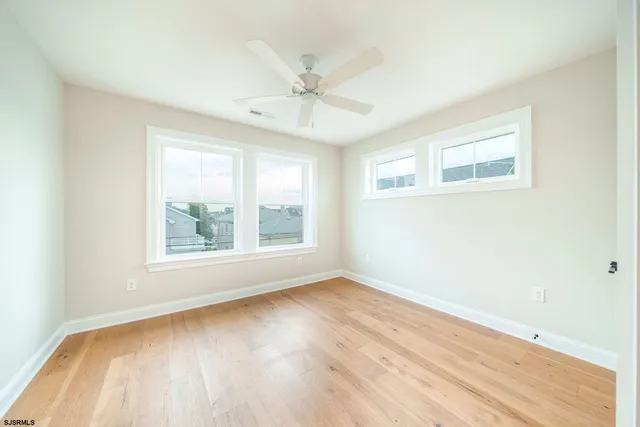 an empty room with wooden floor windows and fan