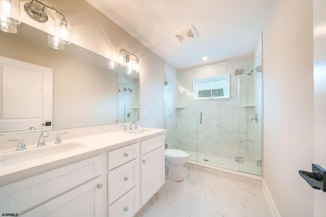 a bathroom with a granite countertop sink a toilet a mirror and shower
