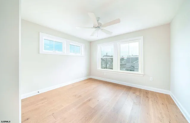 an empty room with wooden floor windows and fan