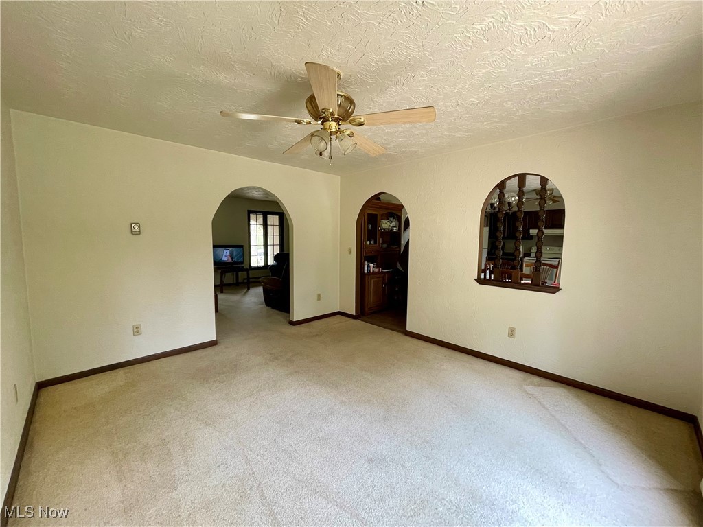 1995 Claus Road Vermilion, OH 44089 - Photo 9 of 21 Unfurnished room featuring arched walkways, a textured ceiling, carpet, a ceiling fan, and baseboards