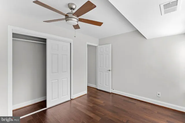 an empty room with wooden floor ceiling fan and windows