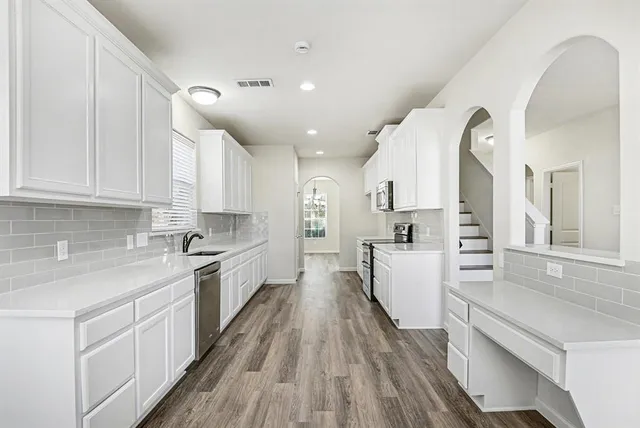 a kitchen with stainless steel appliances granite countertop a stove top oven a sink dishwasher and a refrigerator with wooden floor