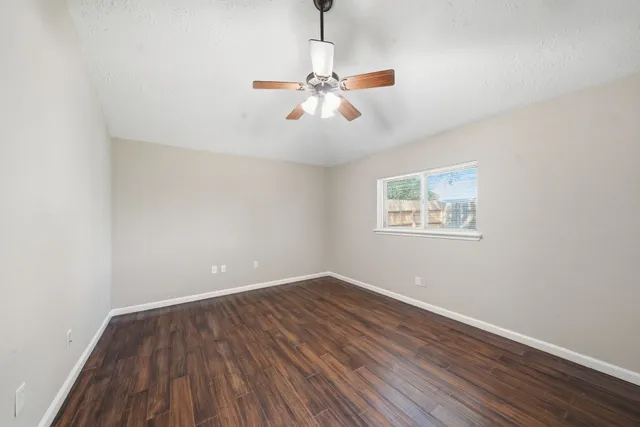 an empty room with wooden floor chandelier fan and windows