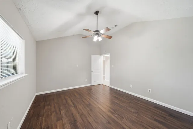 an empty room with wooden floor fan and windows