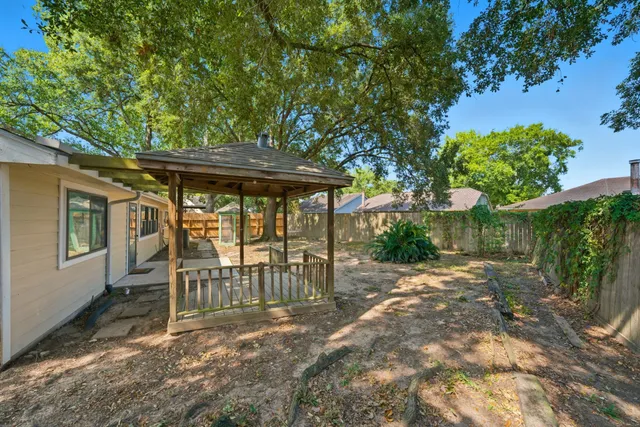 a view of a patio with table and chairs under an umbrella with large trees