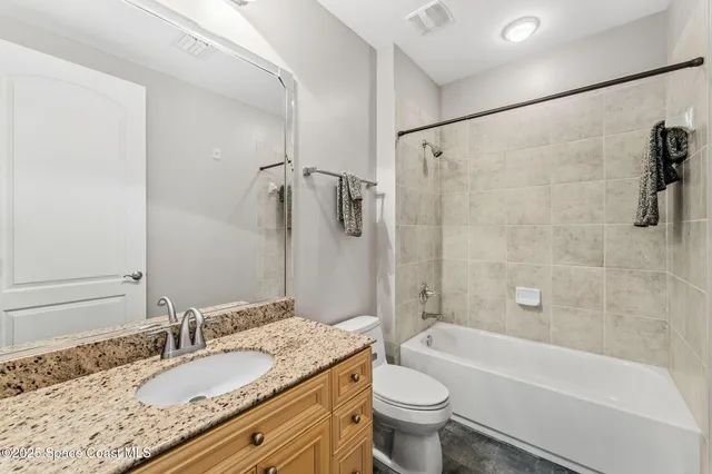 a bathroom with a granite countertop bathtub shower sink vanity mirror and toilet