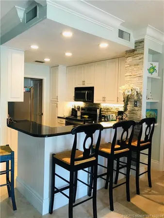 a kitchen with stainless steel appliances kitchen island granite countertop a dining table chairs and a refrigerator