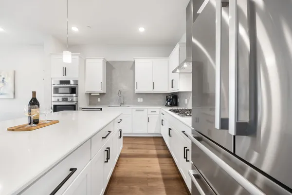 a kitchen with stainless steel appliances kitchen island granite countertop a stove a sink a refrigerator and white cabinets with wooden floor