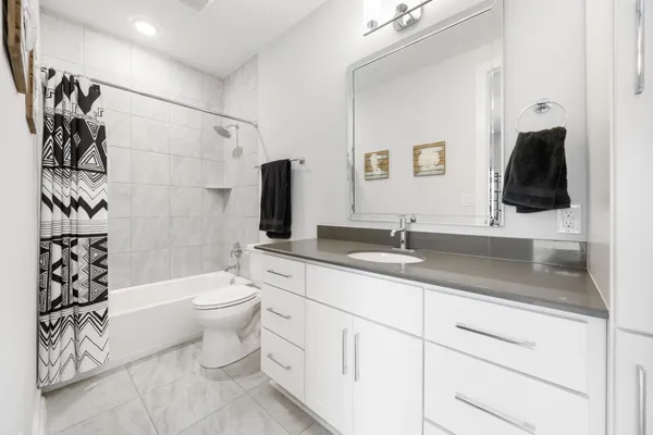 a bathroom with a granite countertop sink a toilet a mirror a bathtub and shower