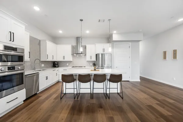 a large white kitchen with lots of counter top space a sink stainless steel appliances and cabinets