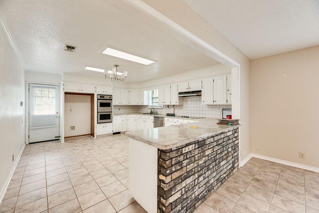 298 Butterfield Road Denison, TX 75021 - Photo 21 of 34 Spacious kitchen area featuring tile flooring, white cabinetry, integrated double wall ovens, a tile backsplash, and a breakfast bar with a brick facade base