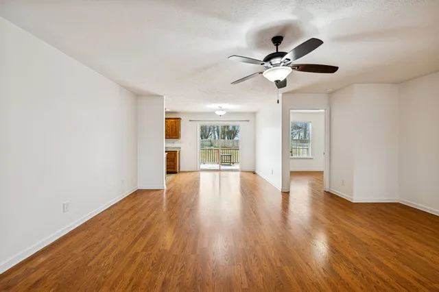 a view of an empty room with chandelier fan and wooden floor