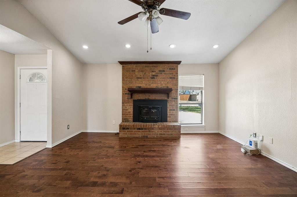 709 Bowie Street Forney, TX 75126 - Photo 8 of 27 an empty room with wooden floor a ceiling fan a fireplace and windows