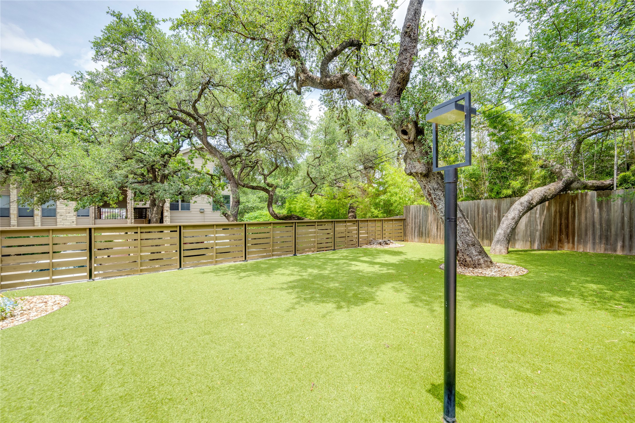 3627 Menchaca Road, Unit 214 Austin, TX 78704 - Photo 24 of 28 A well-maintained yard offers a spacious lawn and mature shade trees, bordered by a modern privacy fence.